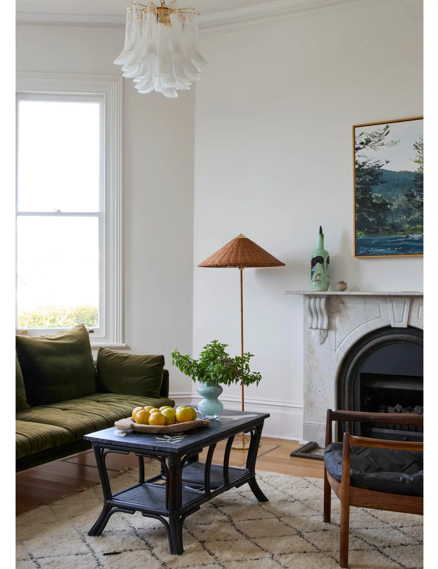 Ljus vardagsrum med grön sammetsoffa, svart soffbord med citroner och växt, vit öppen spis och fönster.