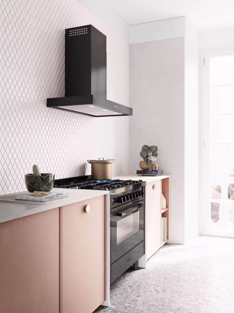 Modern kök med ljusrosa skåp, svart 90 cm ILVE Pro Line spis och köksfläkt, marmormorter, planta och kastrull på spisen. Solen lyser in genom glasdörr till höger.