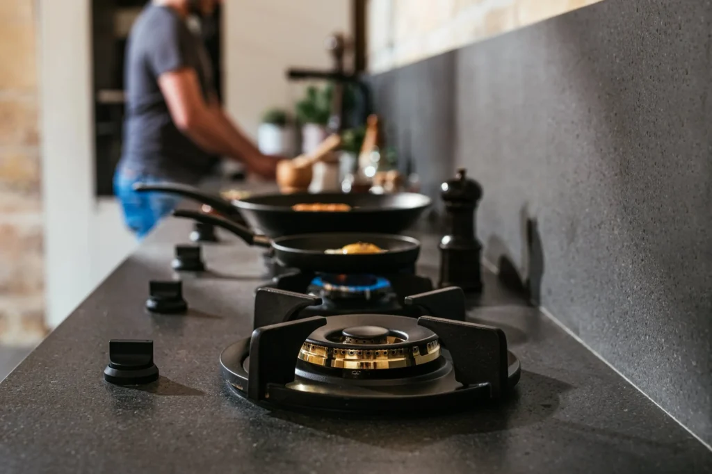 Närbild av PITT Cooking gasbrännare integrerade i mörk bänkskiva med tänd låga